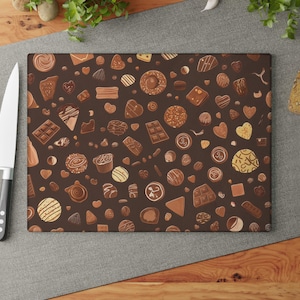 May include: A rectangular chopping board with a dark brown background, patterned with various chocolate sweets in shades of brown and gold. A white-bladed knife and red tomatoes are on the left. Bread, garlic, and herbs are in the background.