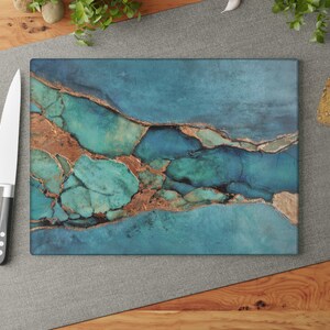 May include: Rectangular cutting board with a turquoise and copper-colored abstract design. The board has a smooth surface and is surrounded by a gray placemat, tomatoes, and a knife.