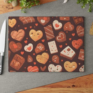 May include: Rectangular cutting board with a dark brown background featuring a pattern of cartoon hearts and chocolate treats in shades of brown, white, and red. The board is surrounded by tomatoes, a knife, and bread.