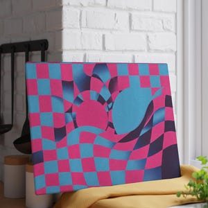 May include: A canvas art piece with a vibrant, abstract design. The artwork features a checkered pattern in shades of pink and blue, with stylized shapes. The piece is displayed on a yellow cloth near a window.