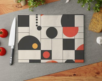 May include: Rectangular cutting board with a geometric design featuring black, red, and yellow shapes on a cream background. The design includes circles, squares, and semi-circles. A knife and tomatoes are next to the board.