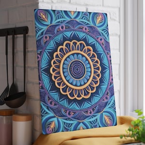 Puede incluir: Impresión rectangular en lienzo con un diseño de mandala detallado. La obra de arte presenta una forma central dorada en forma de flor rodeada de círculos concéntricos en tonos de azul, turquesa y morado. La impresión se muestra sobre una tela amarilla.