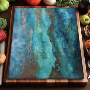 Op de afbeelding: Een rechthoekige snijplank met een blauw en koperkleurig abstract ontwerp. De plank staat op een houten oppervlak, omringd door verse producten, waaronder tomaten, sinaasappels en broccoli. Er is ook een mes aanwezig.