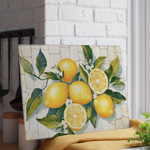 May include: Rectangular cutting board featuring a watercolor illustration of lemons and leaves. The lemons are yellow with green leaves and white flowers. The background is a mosaic pattern. The board is on a yellow cloth.