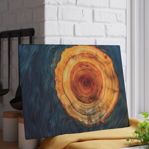 May include: A rectangular wooden art piece featuring a cross-section of a tree trunk. The center displays warm orange and brown tones, surrounded by blue resin. The artwork is displayed on a yellow cloth near a window.