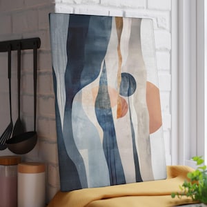 May include: Abstract art print featuring a design of flowing shapes in shades of blue, beige, and orange. The artwork is displayed on a rectangular canvas, leaning against a white brick wall. The color palette is neutral and calming.