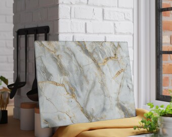 May include: A rectangular cutting board with a marble design. The board features a white and gray background with gold veining. It rests on a yellow cloth near a window and a brick wall. Kitchen decor.