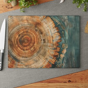 May include: A rectangular cutting board with a wood grain design, featuring concentric circles in shades of brown and orange. One side has a teal-colored accent. A stainless steel knife and red tomatoes are on the gray surface.
