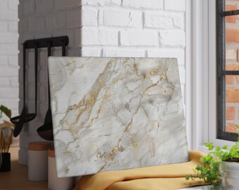May include: Rectangular marble-patterned cutting board with gold veining. The board rests on a yellow cloth, with a white brick wall and a window in the background. Kitchen utensils hang on the wall.
