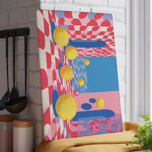 Könnte beinhalten: Ein rechteckiger Kunstdruck mit einem farbenfrohen abstrakten Design. Das Kunstwerk zeigt gelbe Kugeln, blaue Formen und rosa und rote geometrische Muster. Der Druck wird auf einer Küchentheke in der Nähe eines Fensters angezeigt.