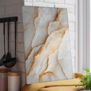May include: A rectangular cutting board with a marble-like design. The board features a pattern of white, beige, and brown swirls, resembling natural stone. It is displayed near a window and kitchen utensils.