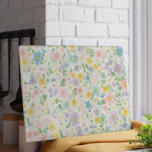 May include: Rectangular cutting board with a floral pattern. The design features a cream background with scattered pastel flowers in shades of pink, blue, yellow, and purple, with green leaves. The board is displayed on a yellow cloth.