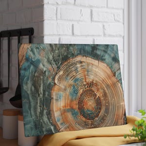 May include: Rectangular cutting board with a wood grain design. The board features concentric circles in shades of brown, orange, and blue, resembling a cross-section of a tree trunk. The board rests on a yellow cloth.
