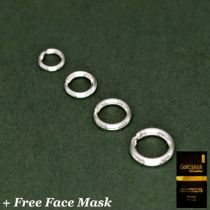 May include: Four silver jump rings of different sizes on a green background. The rings are smooth and have a polished finish.  The text "Gold Mask Luxurious" is visible on a gold and white package in the lower right corner of the image.