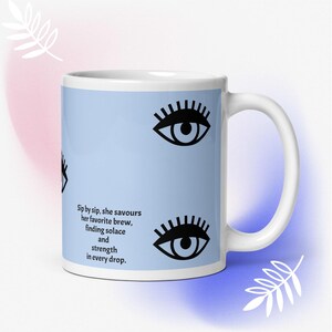 Könnte beinhalten: Eine weiße Keramiktasse mit hellblauem Hintergrund und schwarzen, stilisierten Augen. Die Tasse trägt ein Zitat, das lautet: "Schluck für Schluck genießt sie ihr Lieblingsgetränk, findet Trost und Kraft in jedem Tropfen."