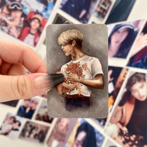 May include: A sticker featuring a drawing of a person with blond hair holding a bouquet of red roses. The person is wearing a white t-shirt with a floral pattern and blue jeans. The background is a gray gradient.