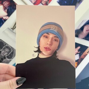 May include: A person with long dark hair is wearing a black turtleneck shirt and a blue and brown beanie with a white logo. The person is looking directly at the camera.