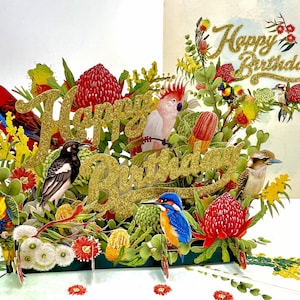 May include: A 3D birthday card with a floral and bird theme. The card features a gold glitter "Happy Birthday" message, surrounded by colorful birds and flowers. Birds include a red parrot, a magpie, and a blue kingfisher.