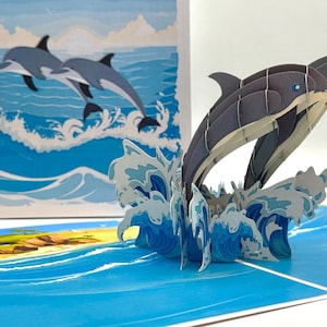 Tarjeta de felicitación emergente en 3D con pareja de delfines nadando en el océano. Tarjetas pop-up de origami hechas a mano. Compra en línea https://origamipopcards.com/