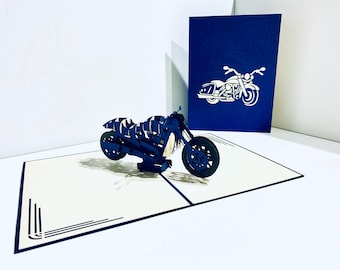 May include: A blue 3D pop-up card featuring a motorcycle. The card is open and the motorcycle is standing upright. The card is on a white surface.