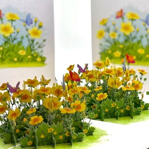 May include: A pop-up greeting card featuring a vibrant display of yellow flowers and green foliage. Colorful butterflies in shades of orange, purple, and blue flutter above the flowers. The card is open, revealing a three-dimensional floral scene.