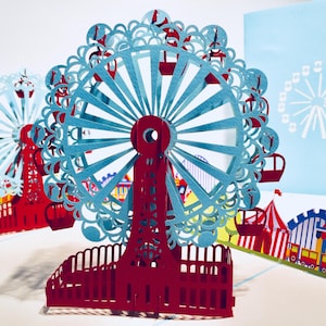 May include: A pop-up card featuring a Ferris wheel design. The Ferris wheel is red and light blue, with intricate cut-out details. The card also includes a carnival scene with tents and rides. A light blue card with a Ferris wheel design is in the background.