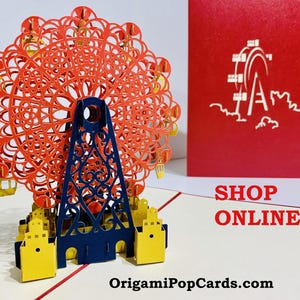 May include: A 3D pop-up Ferris wheel card in orange, yellow, and navy blue. The card is displayed with a red card featuring a Ferris wheel design and the words "SHOP ONLINE". The website OrigamiPopCards.com is also visible.