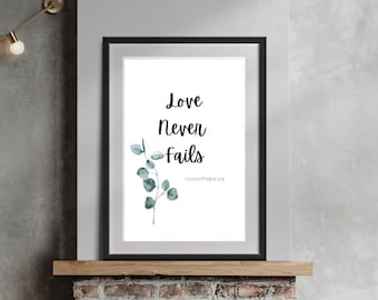 May include: A framed print with a white background and black text that reads "Love Never Fails" with a small sprig of green eucalyptus leaves in the upper left corner. The print is hanging above a brick fireplace with a wood mantle.