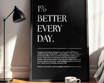 May include: A framed black and white print with the text "1% BETTER EVERY DAY." A coffee cup sits on a floral book in front of the print. The print is leaning against a wall next to a bed with a gray blanket and pillow.