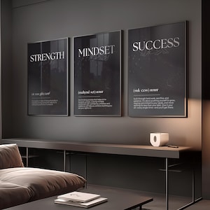 Może przedstawiać: Trzy oprawione plakaty motywacyjne ze słowami "STRENGTH", "MINDSET" i "SUCCESS" w srebrnych literach. Każdy plakat ma czarne tło z białym tekstem definiującym każde słowo. Plakaty są wyświetlane nad ciemnoszarą konsolą.
