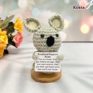 May include: A small crocheted koala holding a sign that reads "Emotional Support Koala. You are braver than you believe, stronger than you seem, smarter than you think and loved more than you'll ever know."