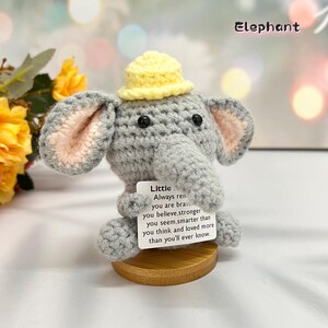 May include: A gray crocheted elephant wearing a yellow hat holds a card with the text "Little Always remember you are brave you believe, stronger you seem, smarter than you think and loved more than you'll ever know."