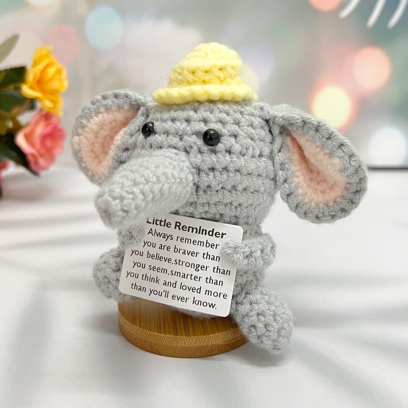 May include: A gray crocheted elephant wearing a yellow hat with a motivational message: "Little Reminder Always remember you are braver than you believe, stronger than you seem, smarter than you think and loved more than you'll ever know."