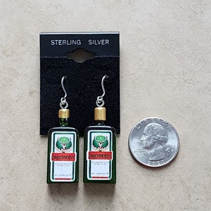 May include: Sterling silver earrings shaped like miniature bottles of Jagermeister liqueur. The bottles are green with gold tops and feature the Jagermeister logo and stag.