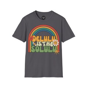 Puede incluir: Camiseta gris oscuro con un diseño retro de arcoíris y el texto "DELULU IS THE SOLULU". El diseño incluye un corazón, una abeja, una flor y un sol sonriente. Una camiseta gráfica informal.