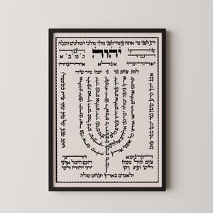May include: A framed print featuring Hebrew text in black ink on a beige background. The text is arranged in a circular and rectangular pattern, with decorative borders. The frame is black.