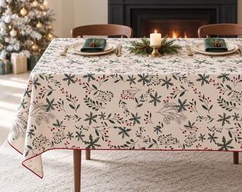 May include: A rectangular tablecloth with a cream-coloured base featuring a repeating pattern of dark green pine branches, holly leaves, and small red berries. The edges are finished with a thin red border, and the fabric drapes over a table.