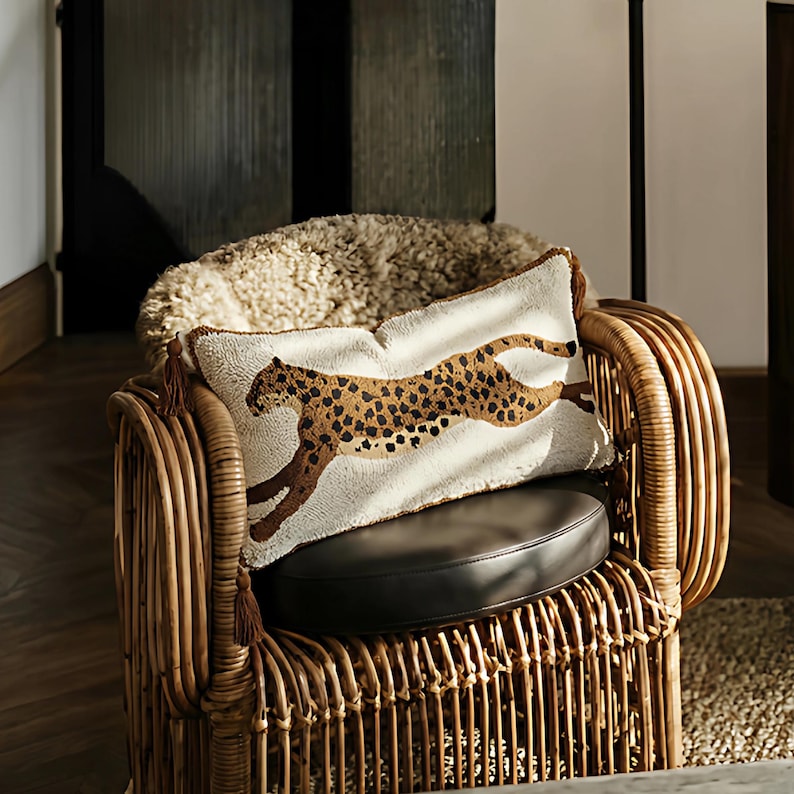May include: A rectangular cushion featuring a cheetah design with brown spots on a cream background. The cushion rests on a dark brown leather seat of a wicker chair. Brown tassels adorn the corners.