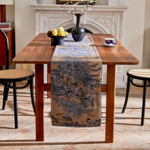 May include: A brown wooden table with a beige table runner featuring a jungle scene with a leopard, toucans, and foliage. The table runner has a blue and white pattern.