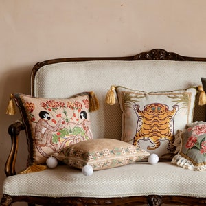 Könnte beinhalten: Ein weißes Sofa mit drei Kissen. Die Kissen haben verschiedene Muster, darunter Affen, einen Tiger und Blumenmuster. Das Sofa ist aus Stoff und hat einen Holzrahmen.