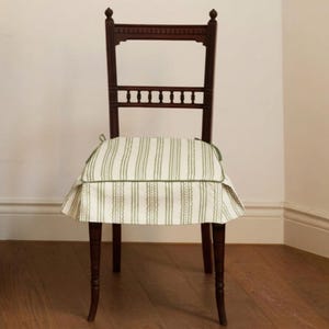 Puede incluir: Silla de madera oscura con cojín a rayas. La silla tiene un respaldo alto con recortes decorativos y un cojín con falda en un patrón de rayas crema y verde. El cojín está ribeteado con ribete verde. Las patas de la silla son delgadas y ligeramente curvadas.