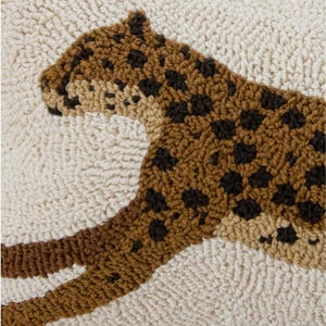 May include: Close-up of a cream cushion cover with a raised tufted leopard design in brown and tan shades, showing dark spotted details and a soft loop-textured surface.