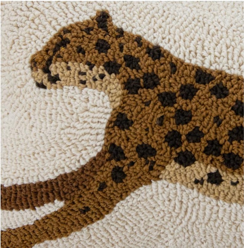 May include: Close-up of a cream cushion cover with a raised tufted leopard design in brown and tan shades, showing dark spotted details and a soft loop-textured surface.