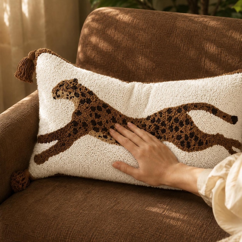 Puede incluir: Un coj&iacute;n rectangular con una base de color crema y un gr&aacute;fico de guepardo marr&oacute;n texturizado y con mechones que recorre el centro. El coj&iacute;n presenta peque&ntilde;as borlas marrones en las esquinas izquierda y derecha, mostrando un dise&ntilde;o detallado de aguja m&aacute;gica.