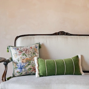 May include: A vintage-style sofa with a white and green patterned upholstery. Two decorative cushions are on the sofa, one with a floral pattern and the other a solid green with white trim.