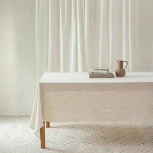 May include: A white linen tablecloth draped over a wooden table with a brown ceramic pitcher and two books stacked on top of each other. The books are titled "PIRANESI" and "THE KLINGER BOOK".