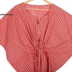 Könnte beinhalten: Roter Kaftan mit weißem Muster und einer Kordelzugtaille. Der Kaftan hat einen V-Ausschnitt und kurze Ärmel.