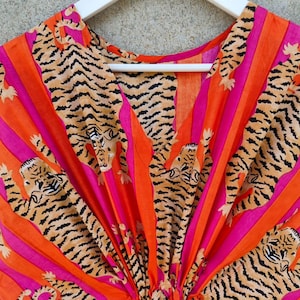 Peut inclure: Un tissu rayé rose et orange avec un imprimé de tigre. Le tissu a un col en V et est froncé en bas.