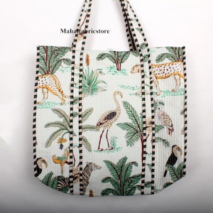 May include: A white canvas tote bag with green and brown stripes on the sides. The bag features a tropical print with leopards, flamingos, toucans, zebras, and palm trees. The text "Mahafabricsstore" is printed on the bag.
