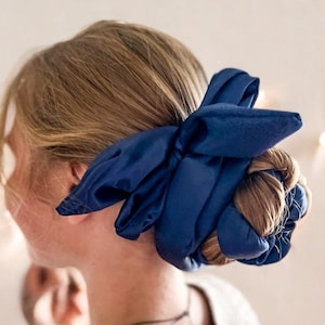 Puede incluir: Una mujer con cabello rubio usando una cinta para el cabello de satén azul marino atada en un lazo.